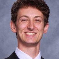 Person smiling wearing a suit in front of a gray wall.